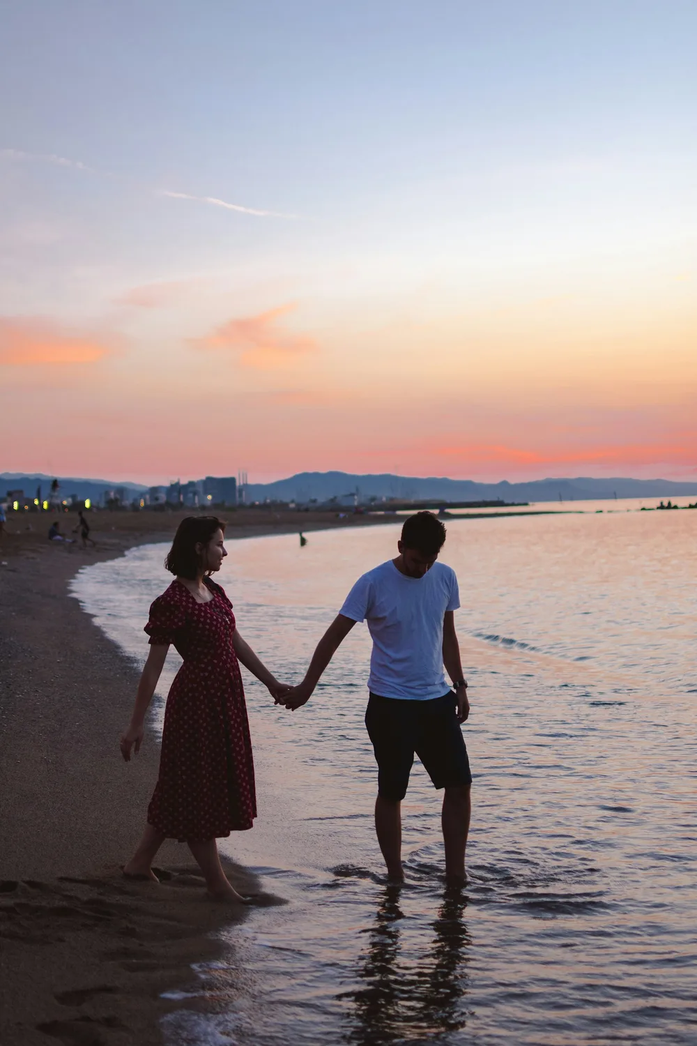 A couple holding hands walking along the shore at sunset